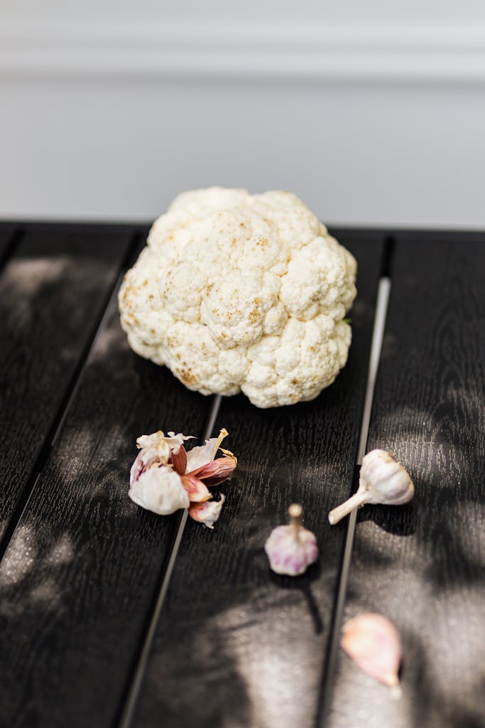 Fresh cauliflower and garlic cloves on a dark wood surface, capturing natural texture and lighting.